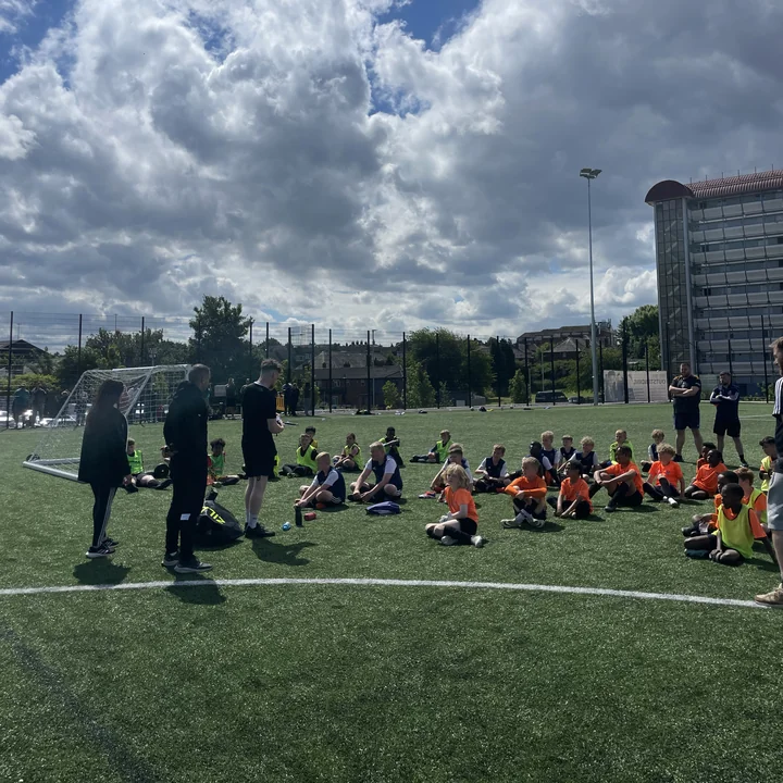 Coach addressing a sitting group of players on the pitch
